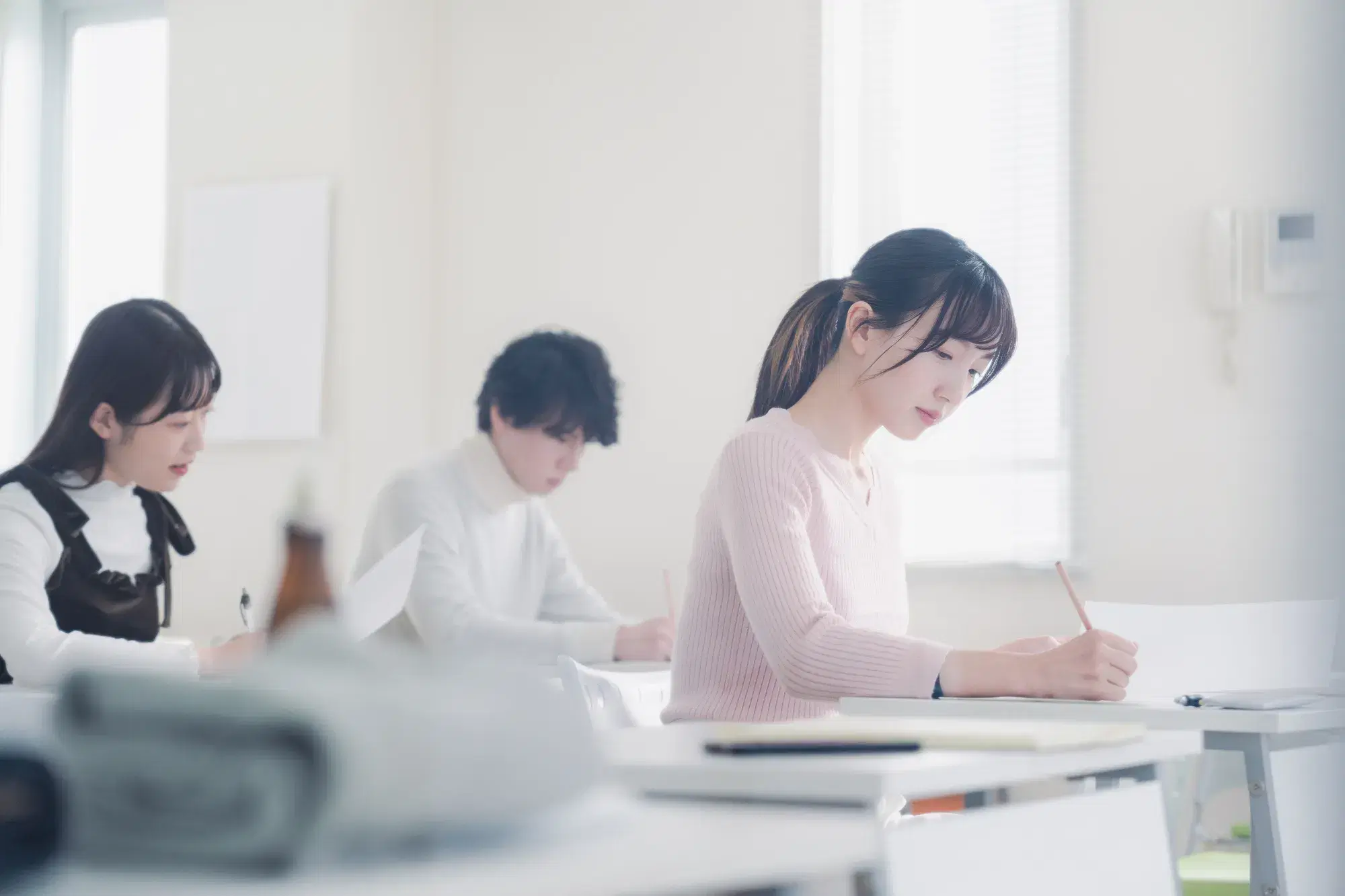 若い女性二人と男性一人が机に向かい勉強している