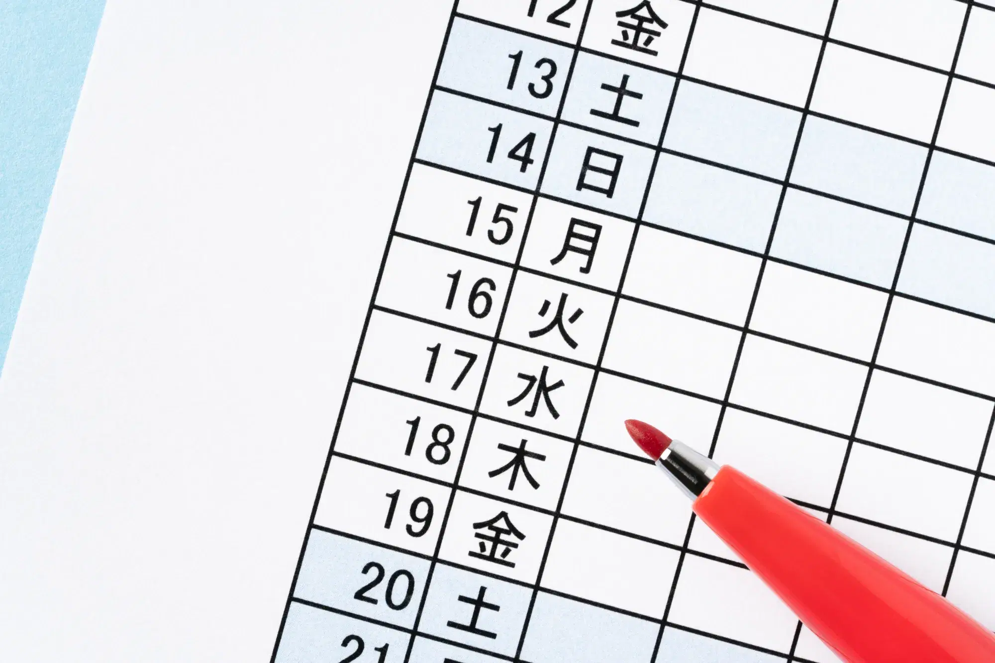 日付と曜日が書かれた表の上に赤色のペンが置かれている様子が写っている。