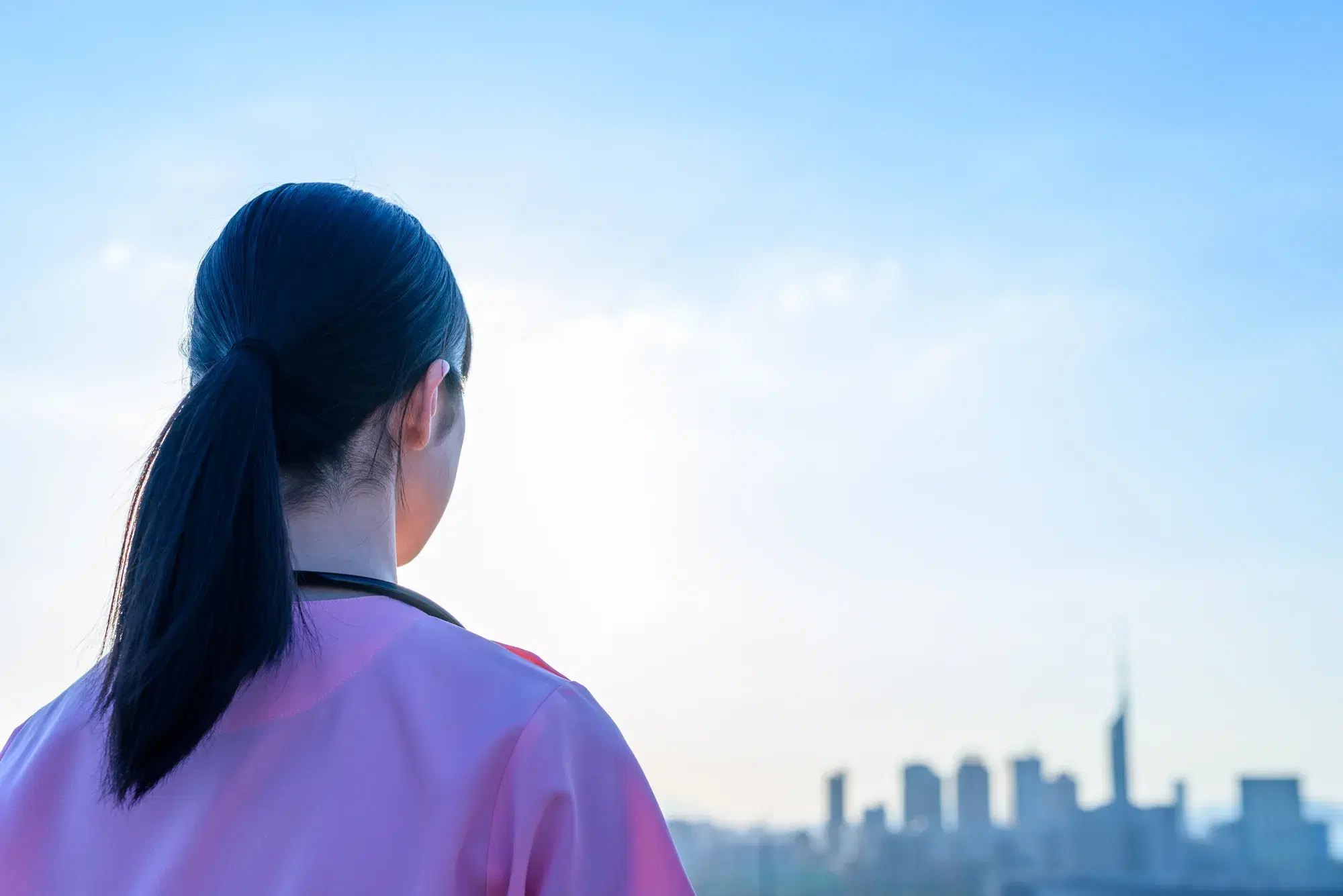 ピンク色の服を着た看護師が遠くの街を見ている