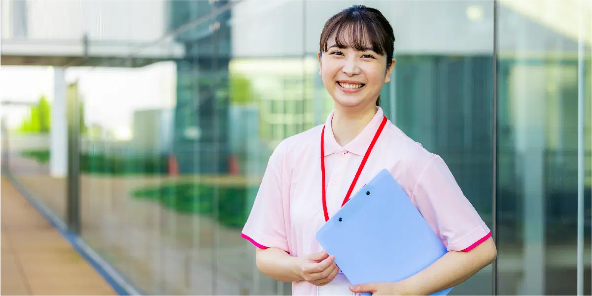 ピンクの服を着て青いバインダーを持ち笑う女性