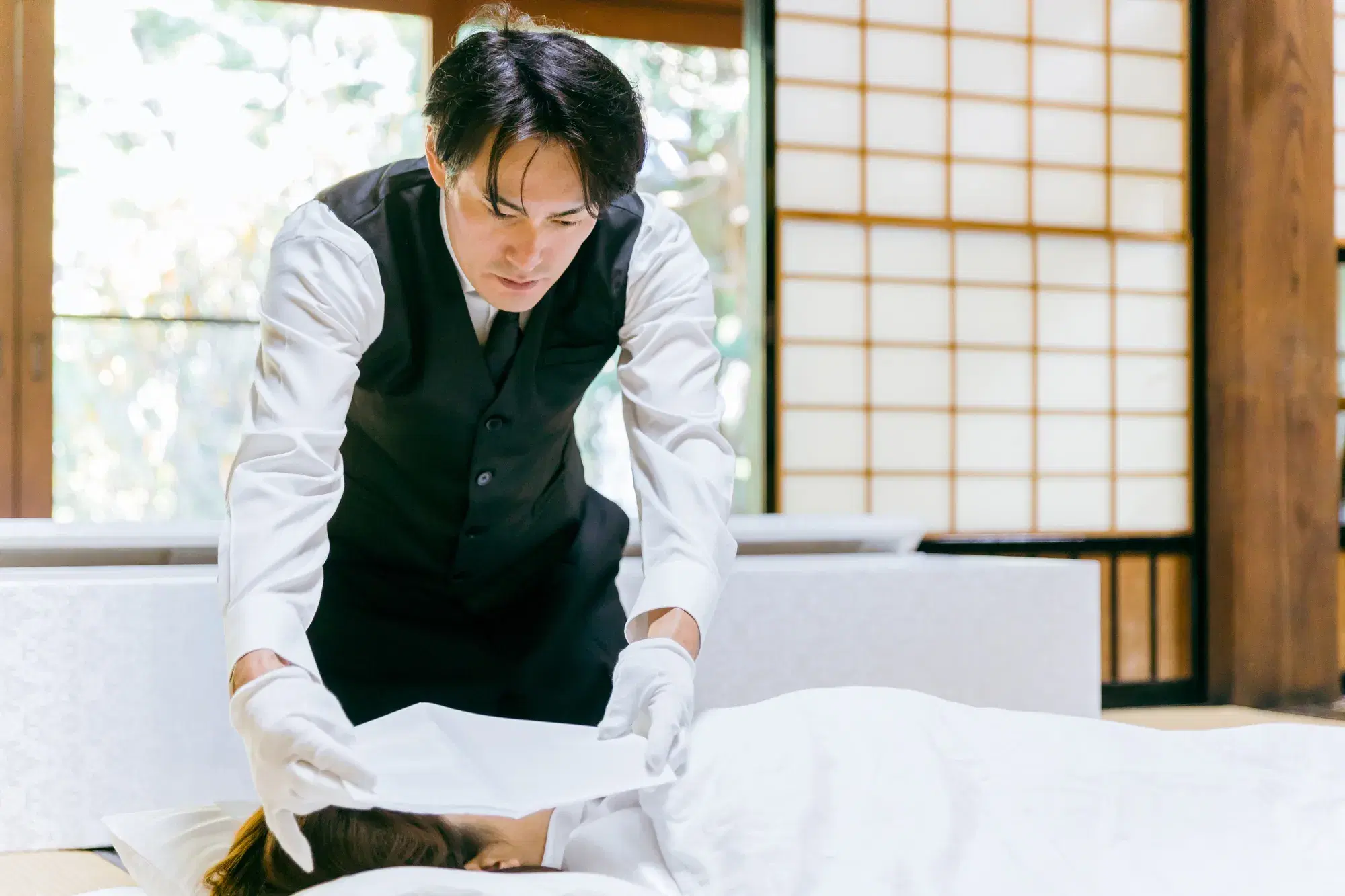 葬儀屋の男性が遺体の顔の上に白い布を被せようとしている。