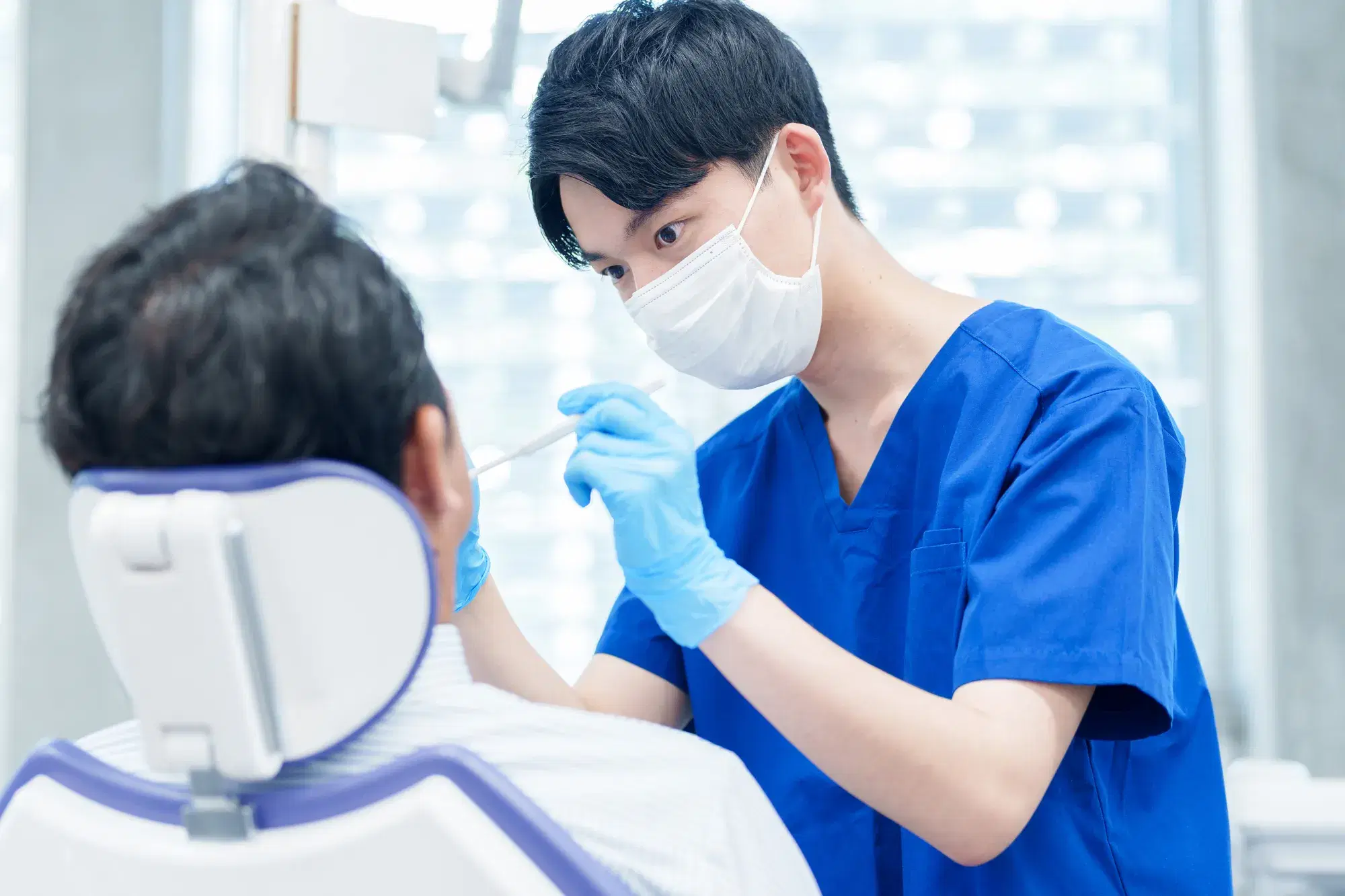 マスクをつけた青い服を着た男性が男性の患者さんの歯の治療をしている
